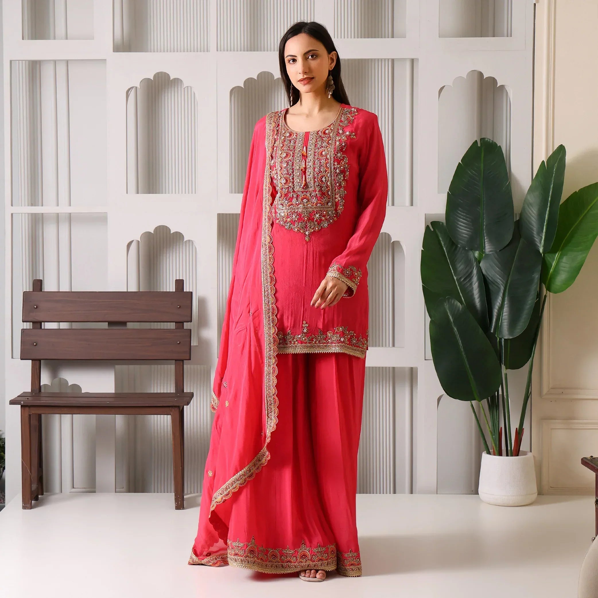 Woman wearing a pink embroidered ethnic suit with dupatta, standing indoors by plants