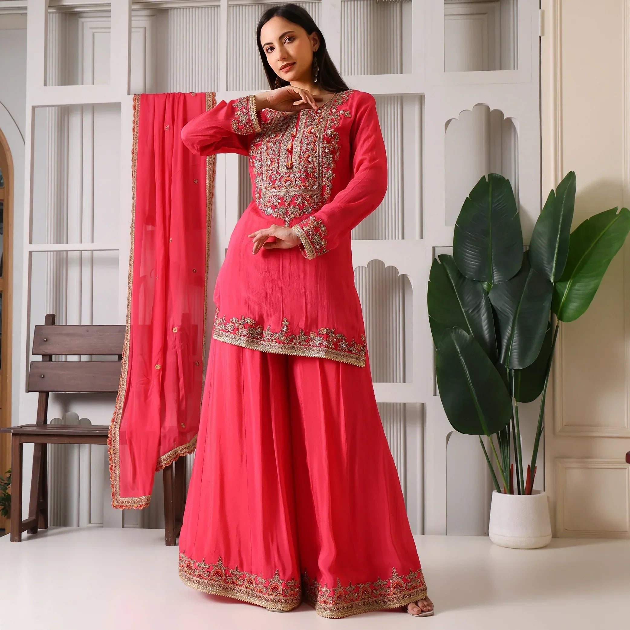 Woman wearing a pink embroidered ethnic palazzo suit set with dupatta indoors