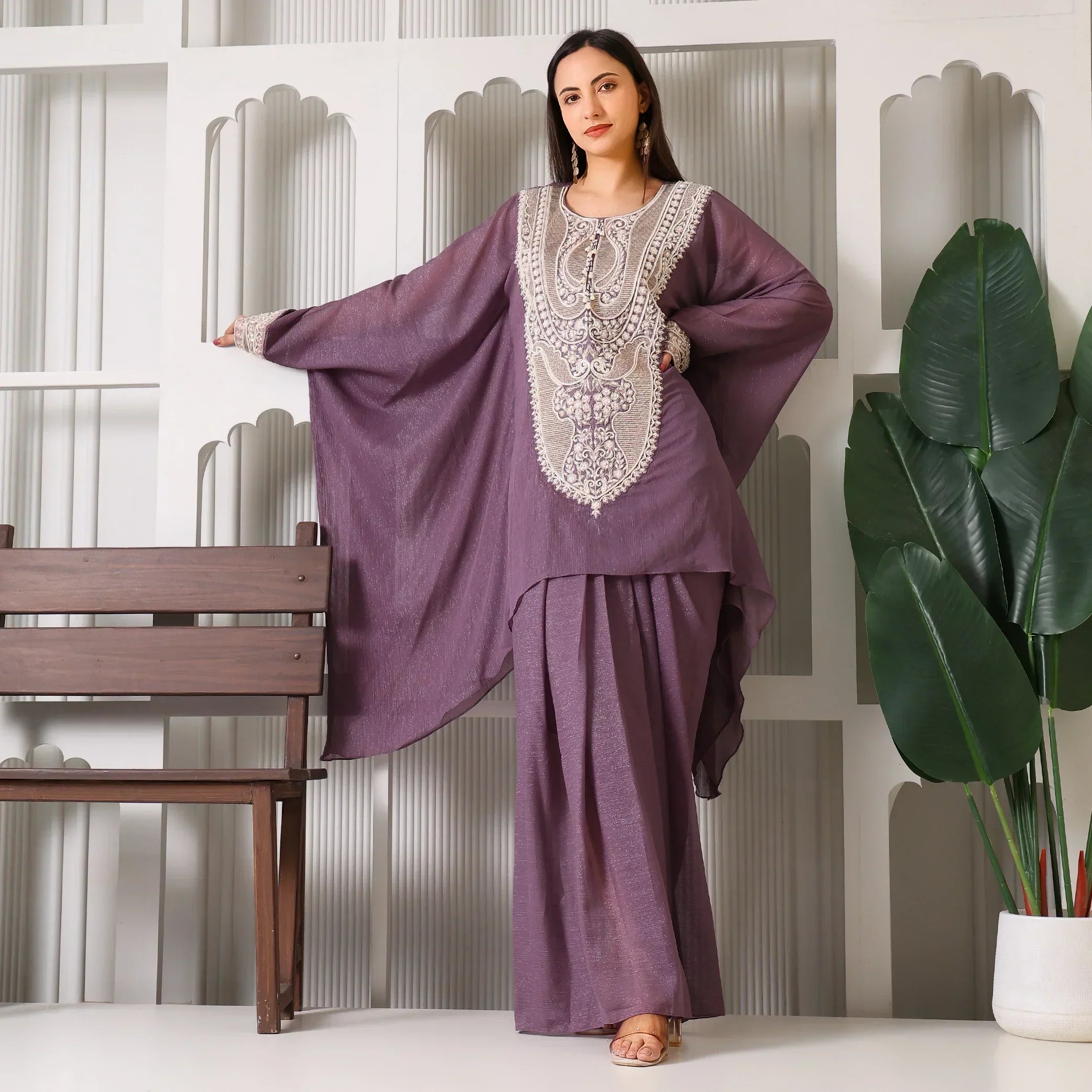 Woman wearing a mauve embroidered ethnic kaftan set, standing indoors by a plant