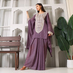 Woman in purple embroidered ethnic suit posing indoors with green plant and wooden bench