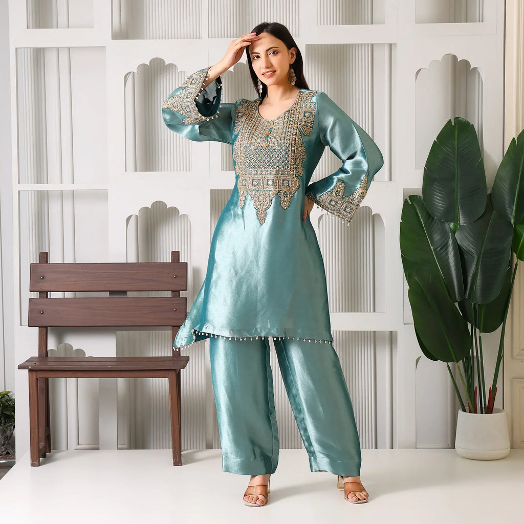 Woman wearing teal embroidered ethnic kurta set with wide pants, standing indoors