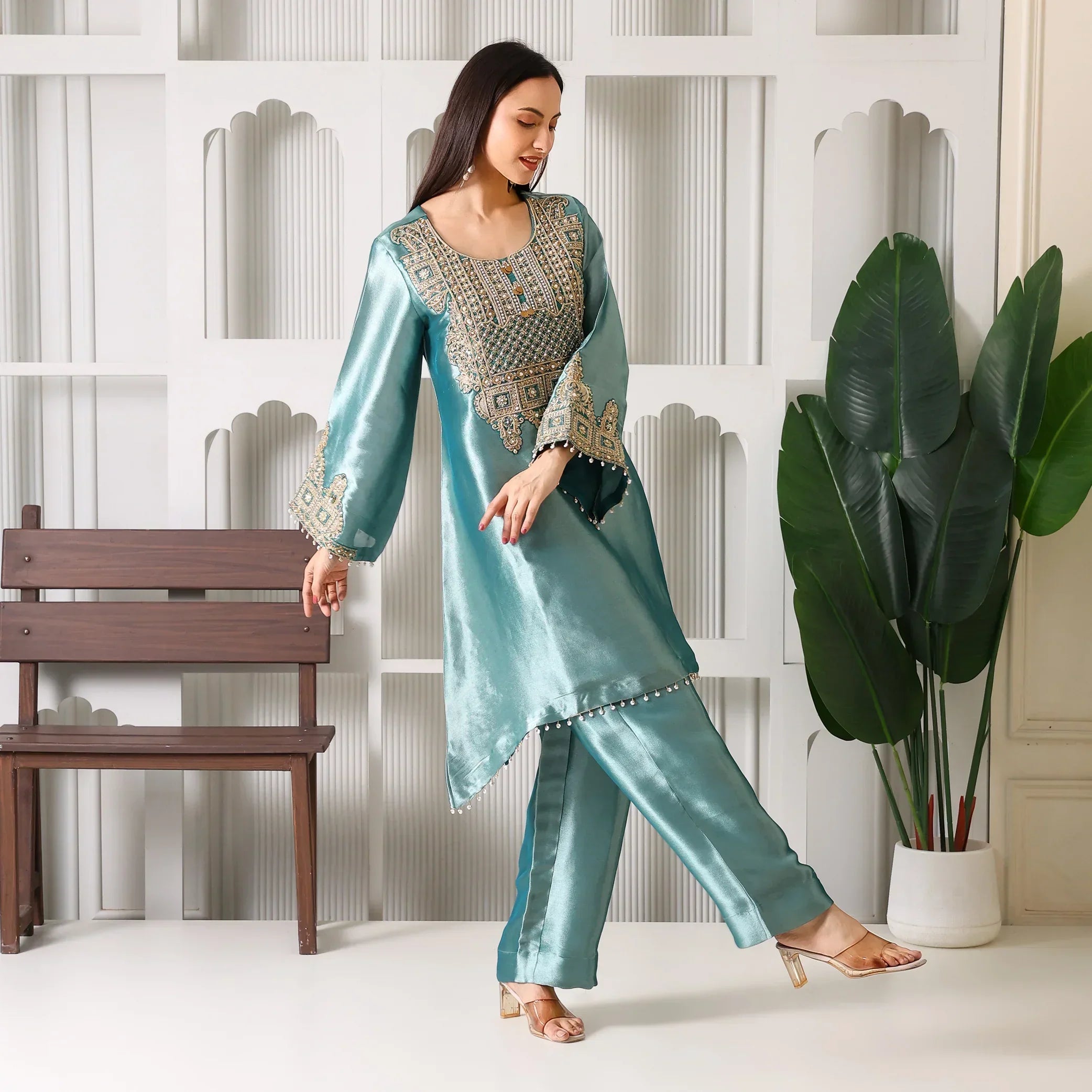Woman in teal silk embroidered ethnic suit set with straight pants, festive wear indoors