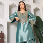 Woman in teal silk kurta with intricate gold embroidery, wearing statement earrings