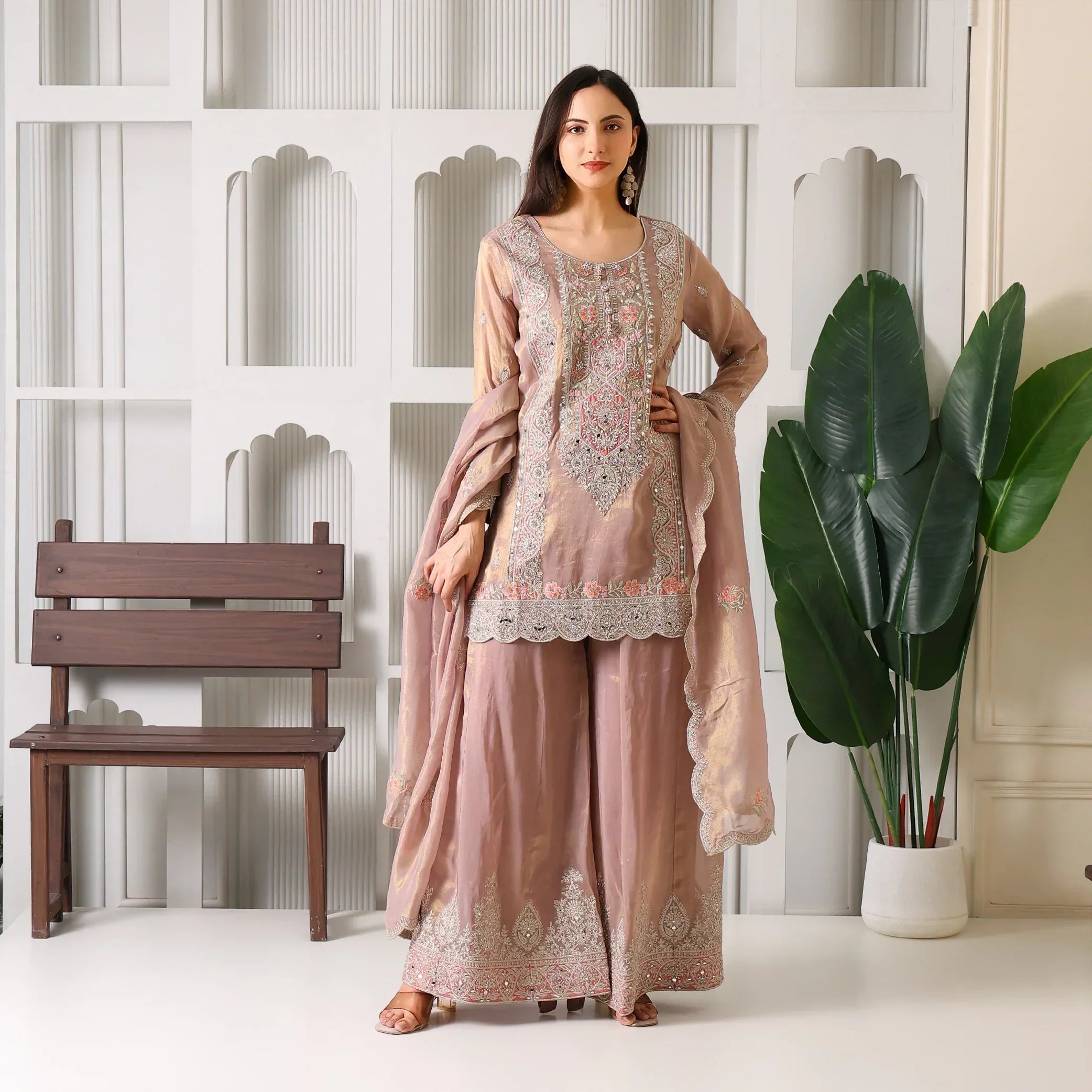 Woman in blush pink embroidered ethnic palazzo suit with dupatta, standing indoors