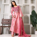 Woman wearing a pink Banarasi Anarkali suit set with embroidery, posed indoors by a bench