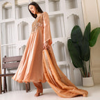 Woman in peach Banarasi Anarkali suit with dupatta, standing indoors near plants