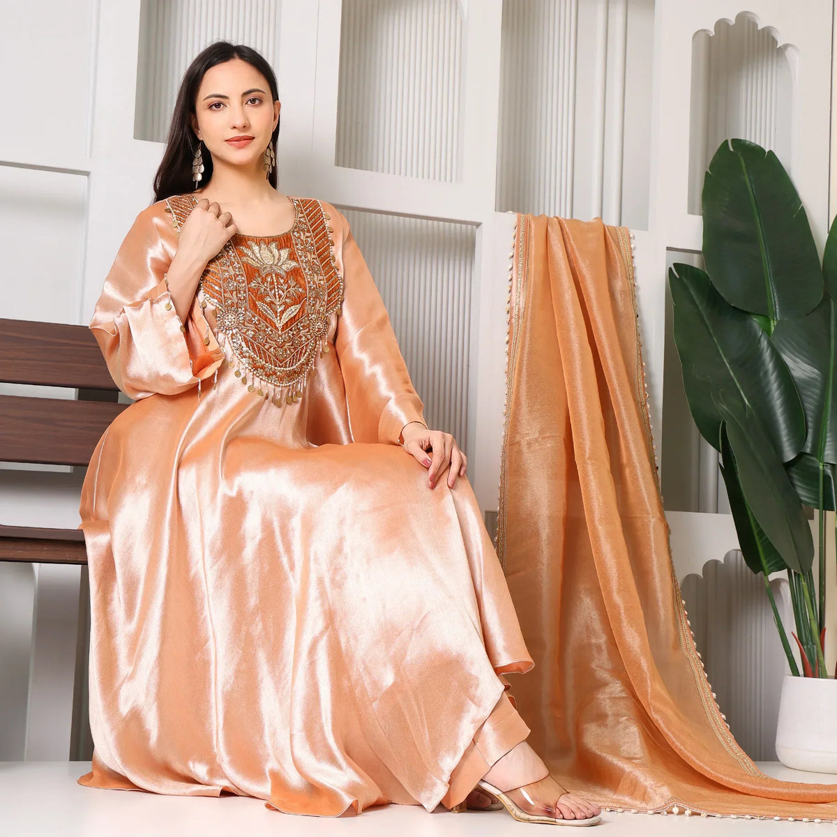 Woman in peach silk ethnic Anarkali suit with intricate golden embroidery, dupatta draped beside her