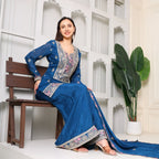 Woman in blue embroidered Anarkali suit with dupatta, sitting on a bench, indoor setting