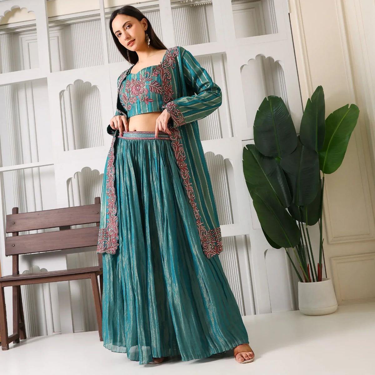 Woman in teal embroidered ethnic three-piece suit set with flared skirt, standing indoors
