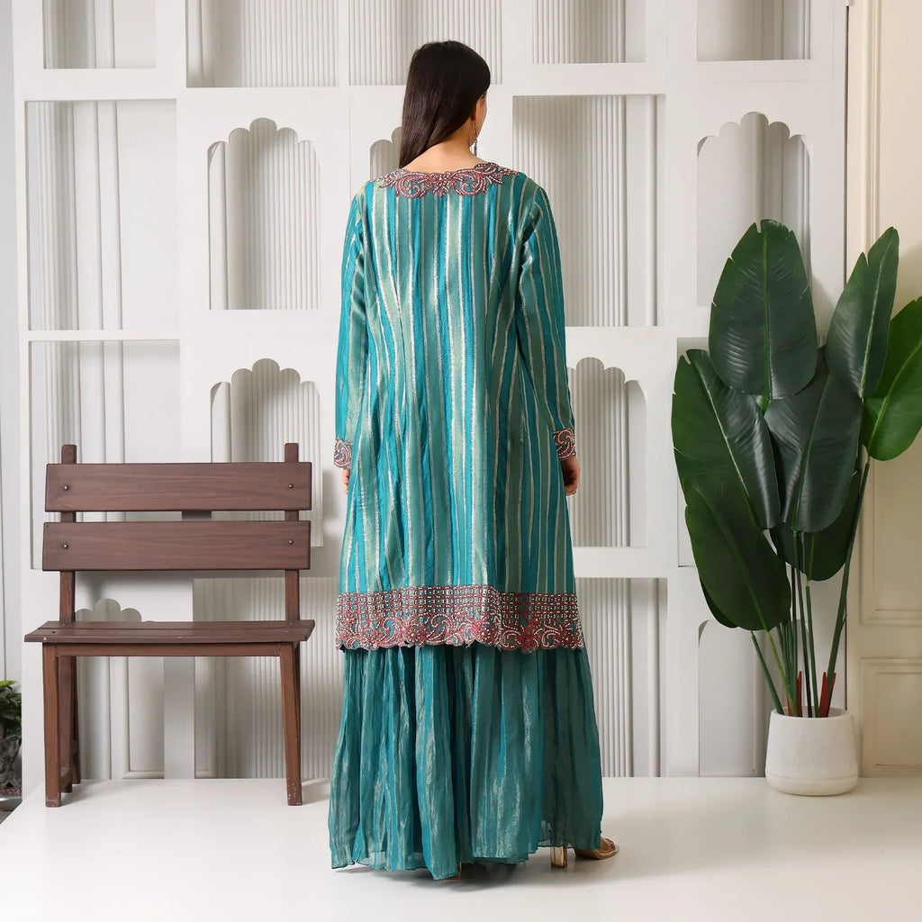 Woman wearing teal striped Anarkali suit with embroidered details, standing indoors