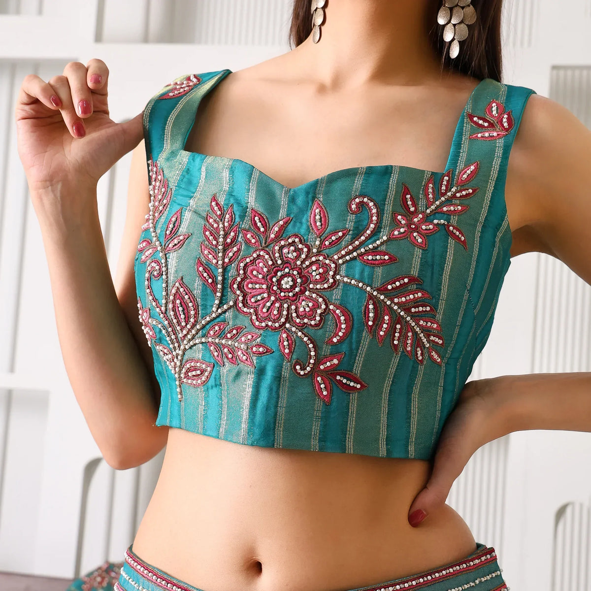 Woman wearing teal ethnic crop top with pink floral embroidery and striped detailing