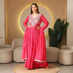 Woman in a vibrant pink embellished Anarkali suit, posing in a modern ethnic living room.