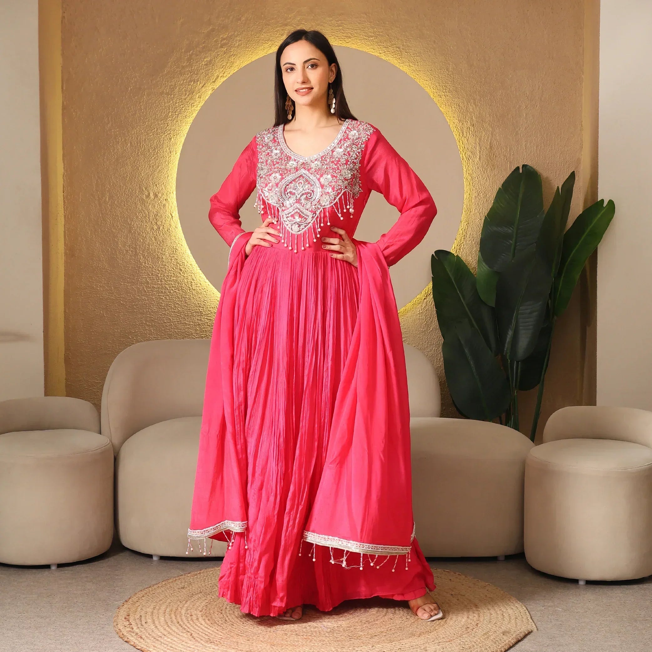 Woman in a vibrant pink embellished Anarkali suit, posing in a modern ethnic living room.