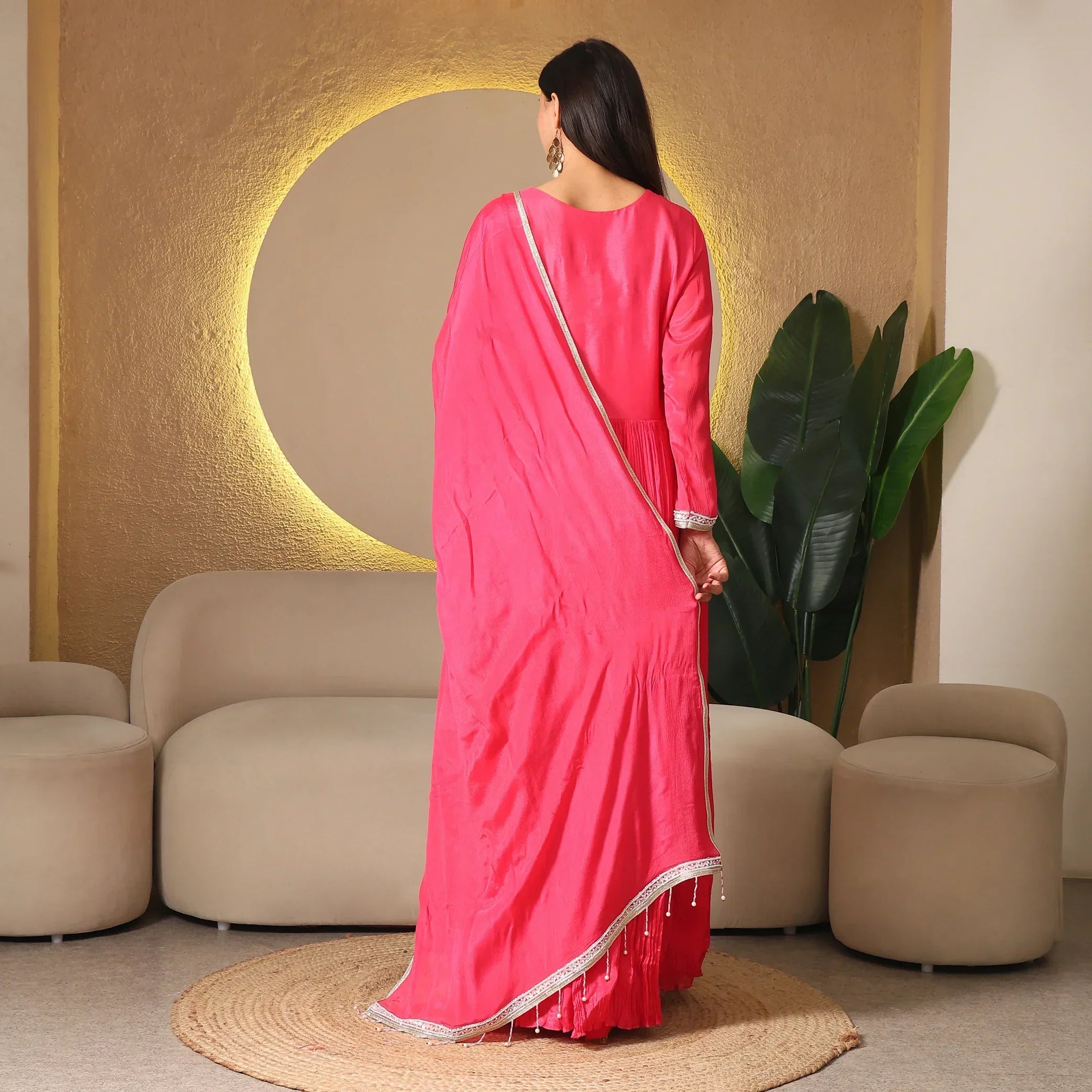 Woman in pink ethnic anarkali suit with dupatta, standing in modern living room