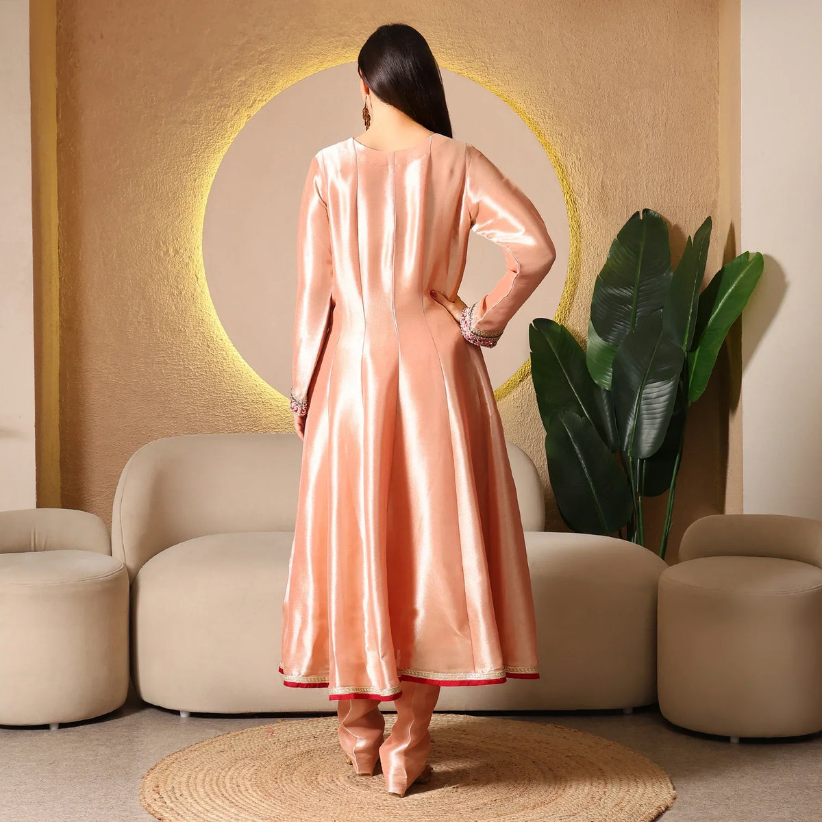 Woman in peach silk Anarkali suit with churidar, standing in modern living room