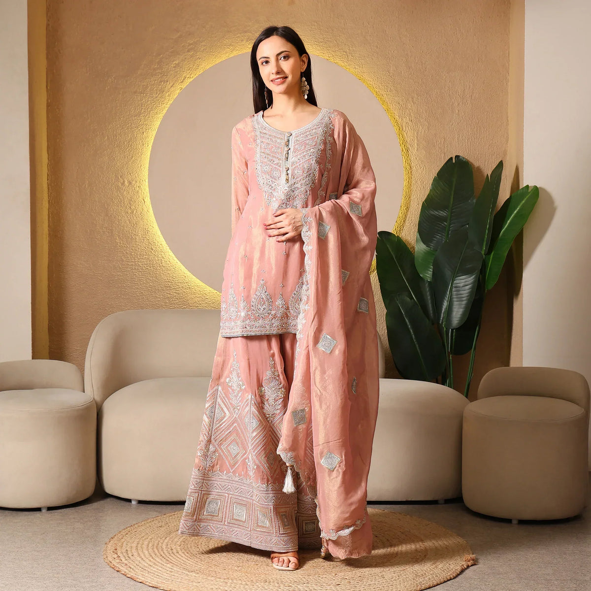 Woman wearing peach embroidered Anarkali suit with dupatta, posing in elegant room.