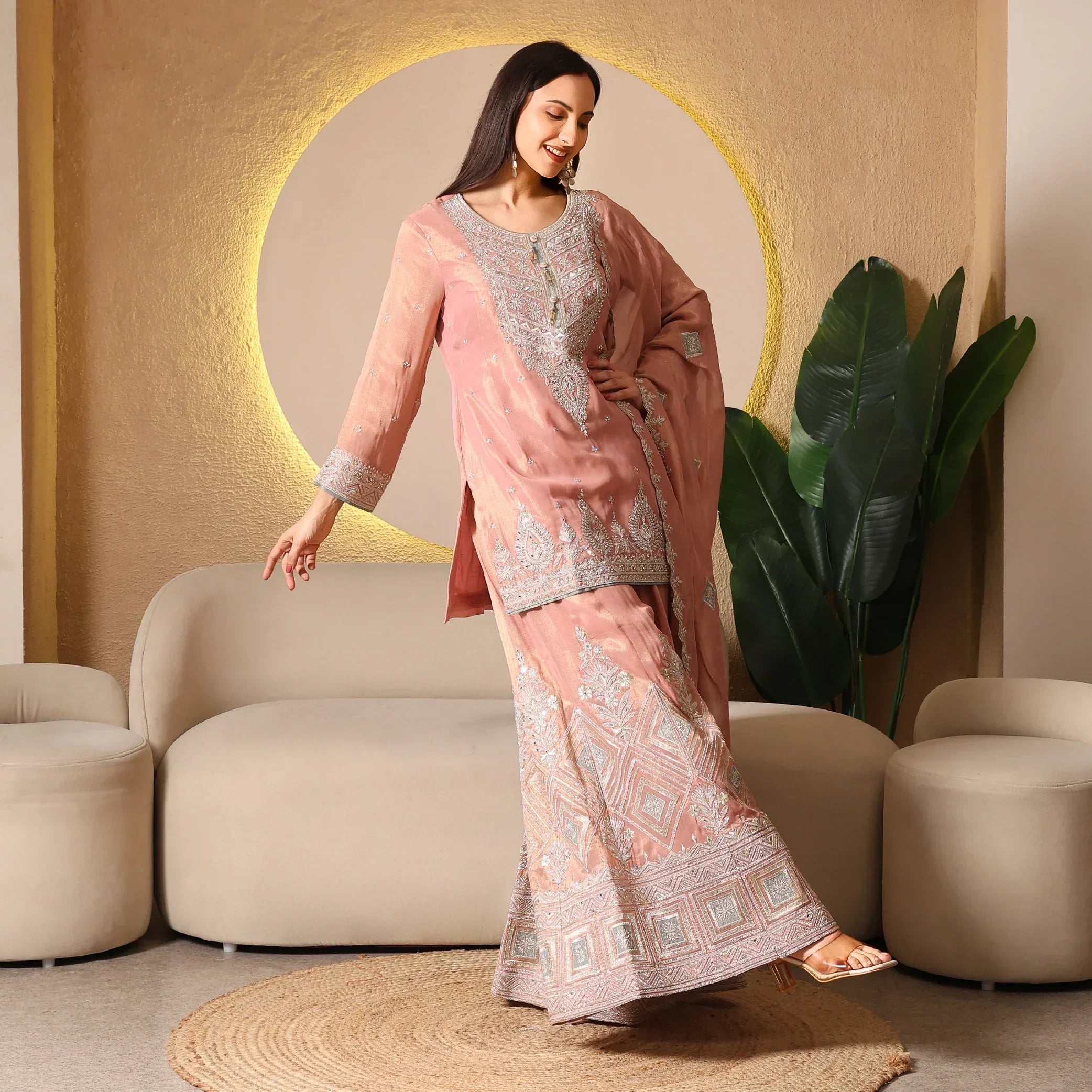 Woman in pastel pink embroidered Anarkali suit with dupatta, posing in modern living room