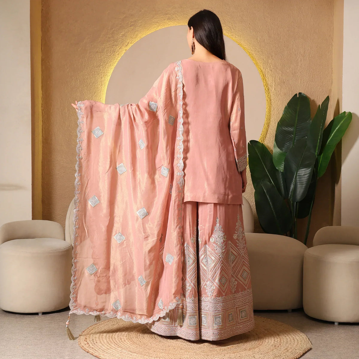 Woman wearing peach embroidered ethnic suit with dupatta, standing in elegant setting