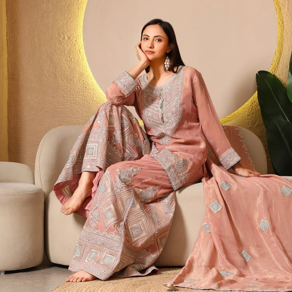 Woman in a blush pink embroidered ethnic suit with dupatta, seated on a sofa