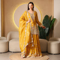 Woman in mustard yellow embroidered ethnic suit with dupatta, standing in modern living room