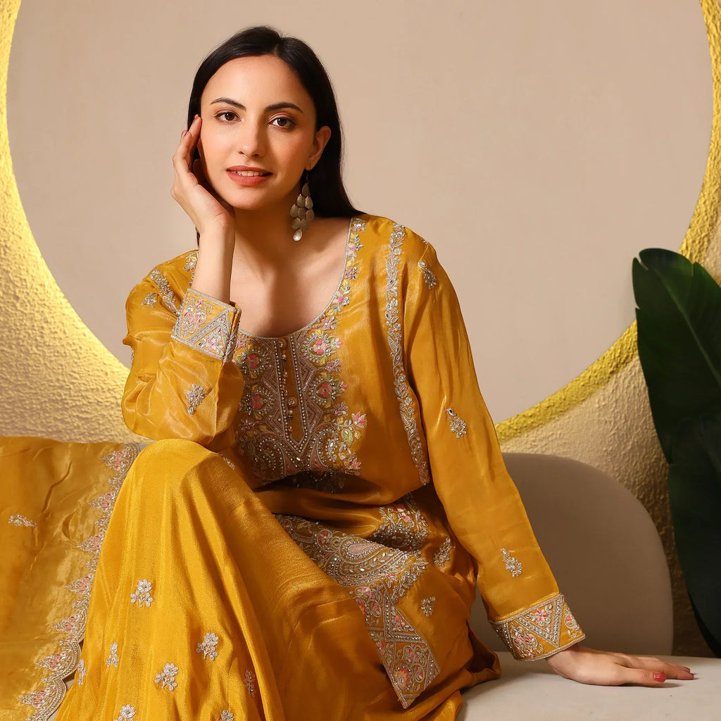 Woman in mustard embroidered ethnic suit with dupatta, sitting indoors, festive look