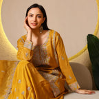 Woman in mustard embroidered ethnic suit with dupatta, sitting indoors, festive look