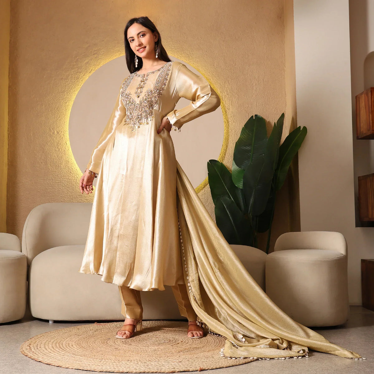 Woman wearing a gold embroidered Anarkali suit with dupatta in a modern living room