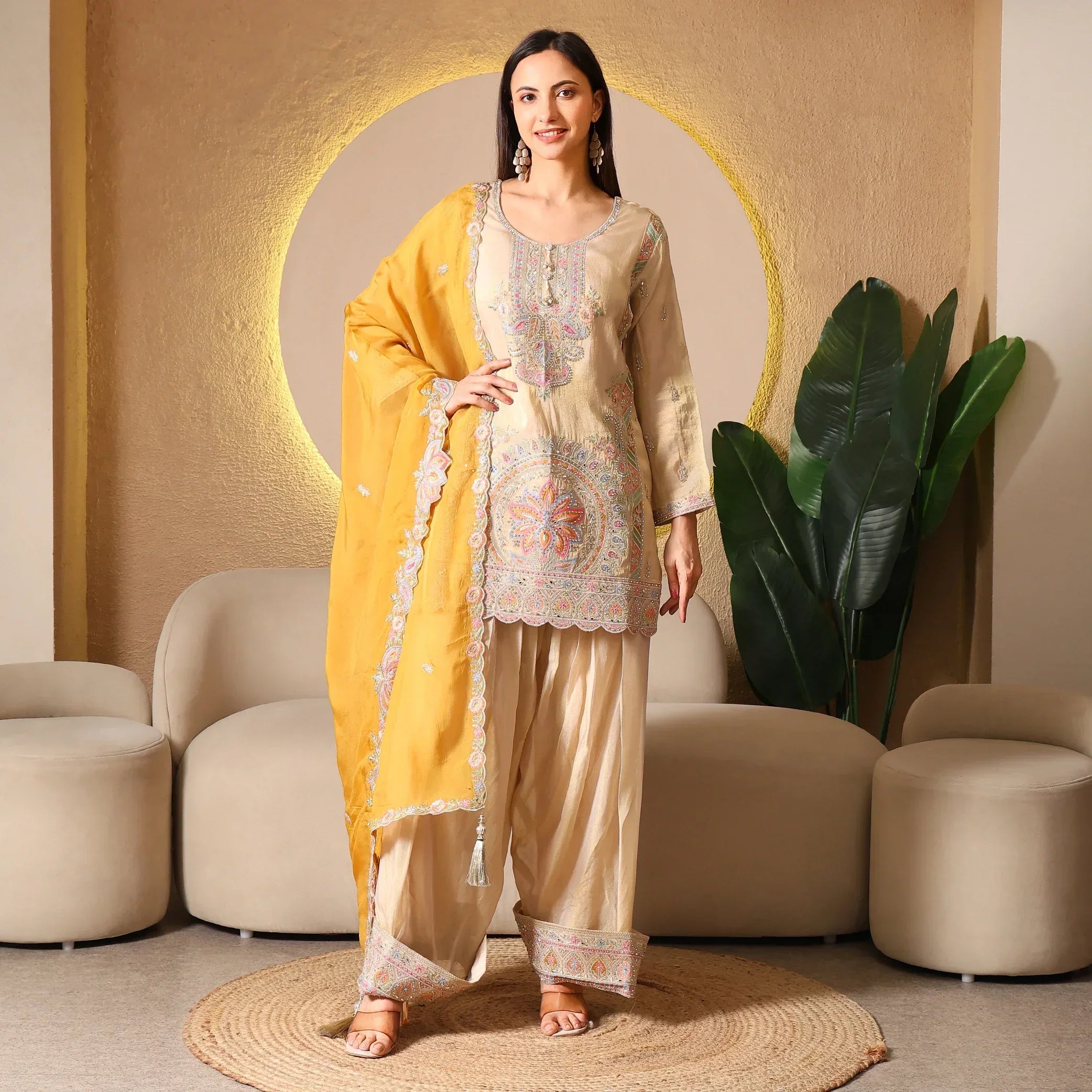 Woman in luxury embroidered beige ethnic suit with yellow dupatta, festive outfit indoors