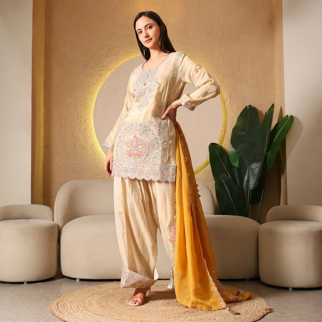 Woman wearing cream embroidered ethnic suit with yellow dupatta, festive outfit indoors
