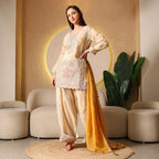 Woman wearing cream embroidered ethnic suit with yellow dupatta, festive outfit indoors
