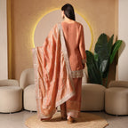 Woman in peach ethnic suit with embellished dupatta, standing in elegant modern interior