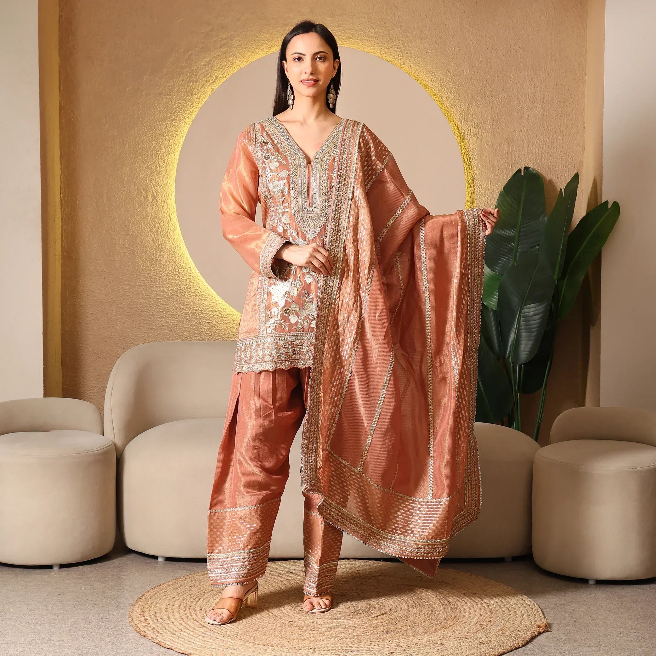Woman wearing a rust silk embroidered ethnic suit set with dupatta, standing indoors