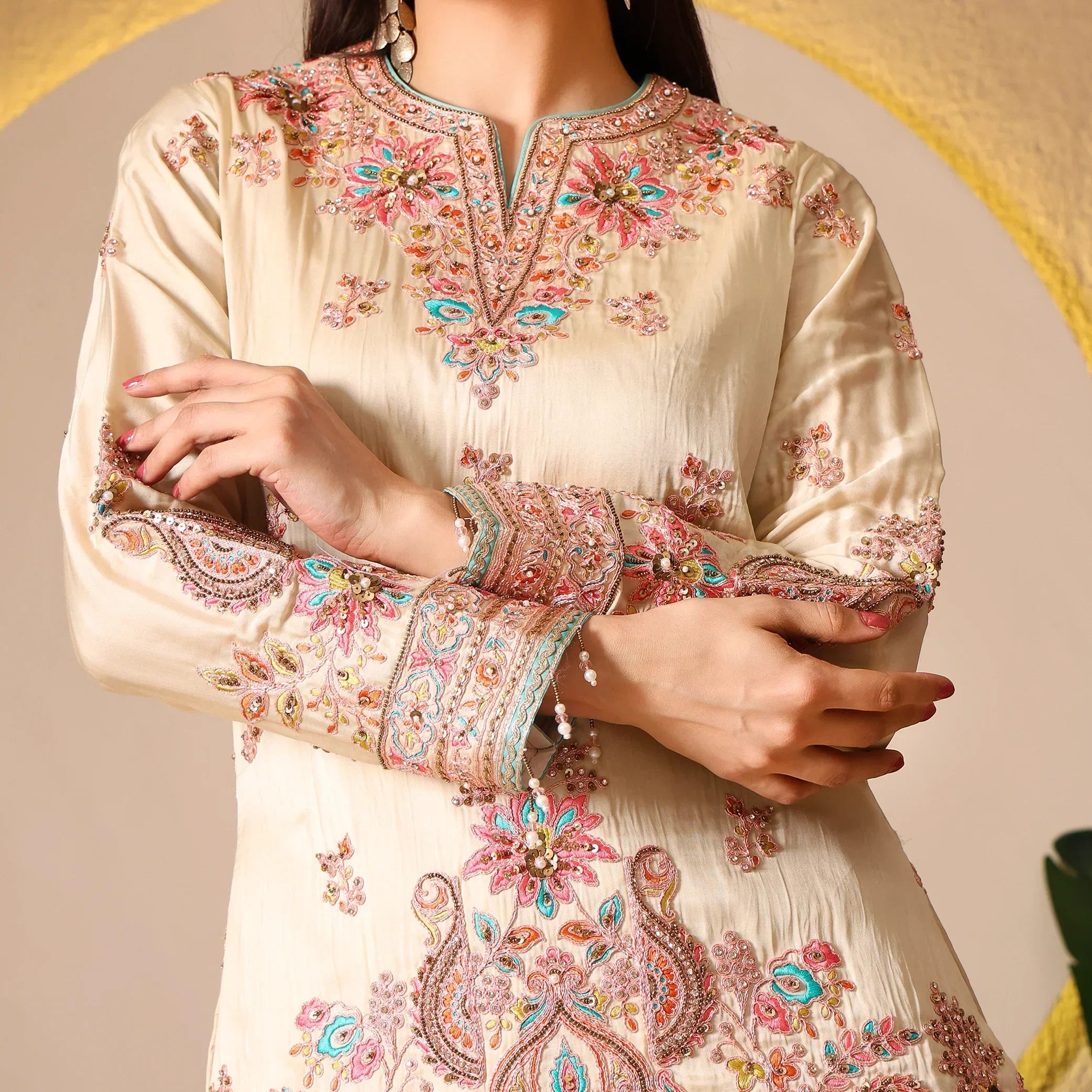 Close-up of woman wearing cream Anarkali suit with pink, gold and turquoise embroidery