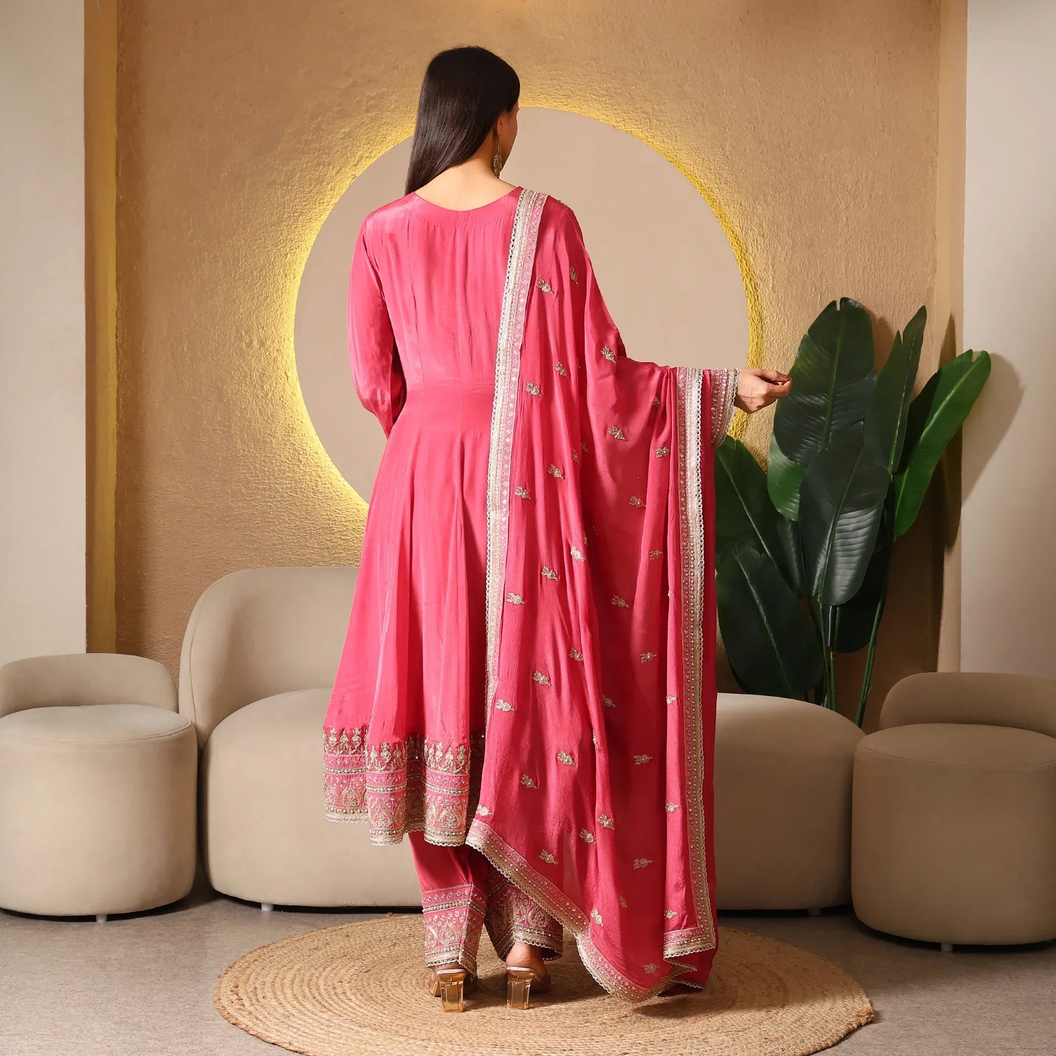 Woman modeling pink embroidered Anarkali suit with dupatta in a modern indoor setting