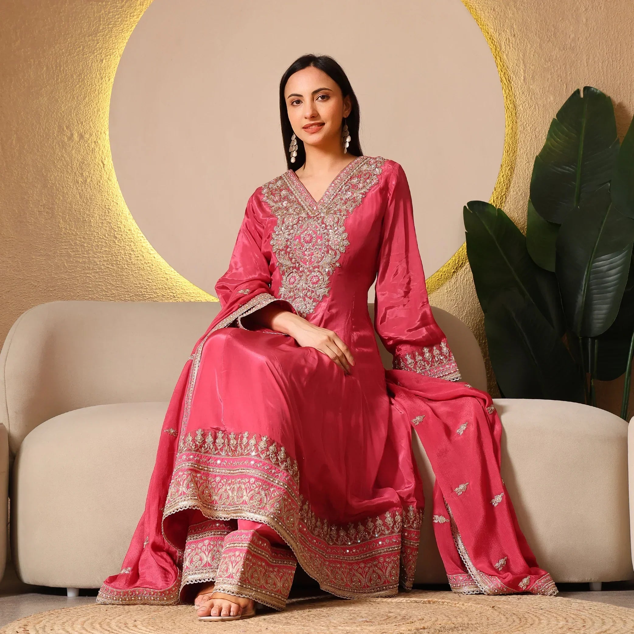 Woman in a pink Banarasi Anarkali suit with gold embroidery, sitting on a sofa