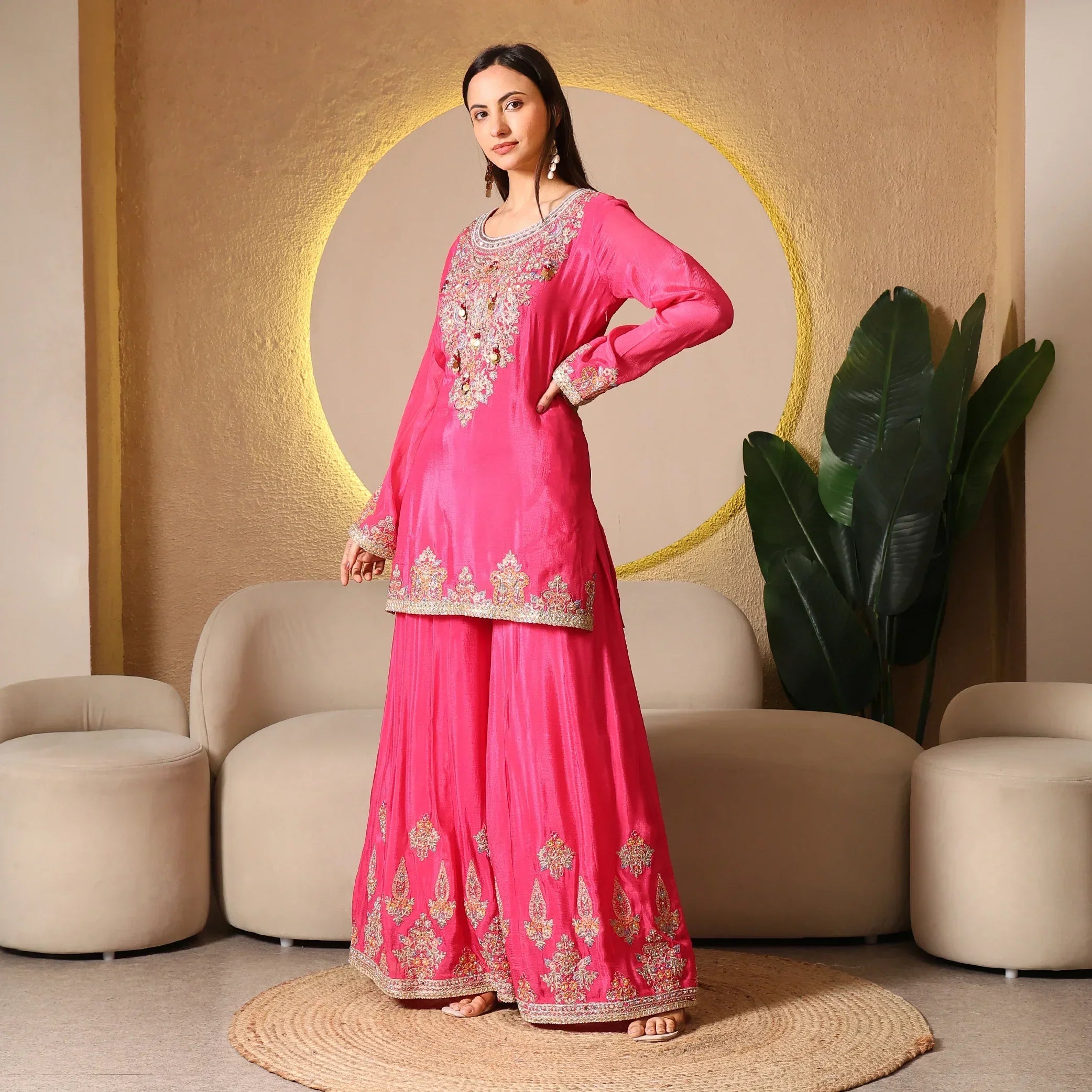 Woman wearing a pink embroidered ethnic suit set, in a modern living room setting