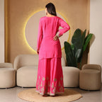 Woman wearing bright pink embroidered ethnic suit set, back view, in modern indoor setting