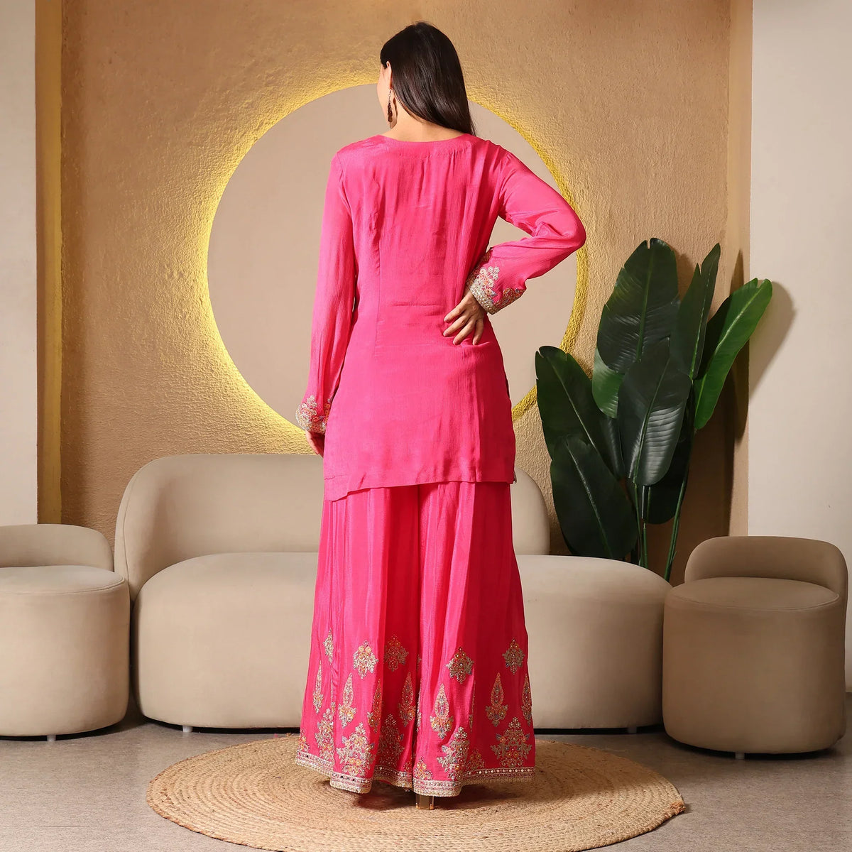 Woman wearing bright pink embroidered ethnic suit set, back view, in modern indoor setting