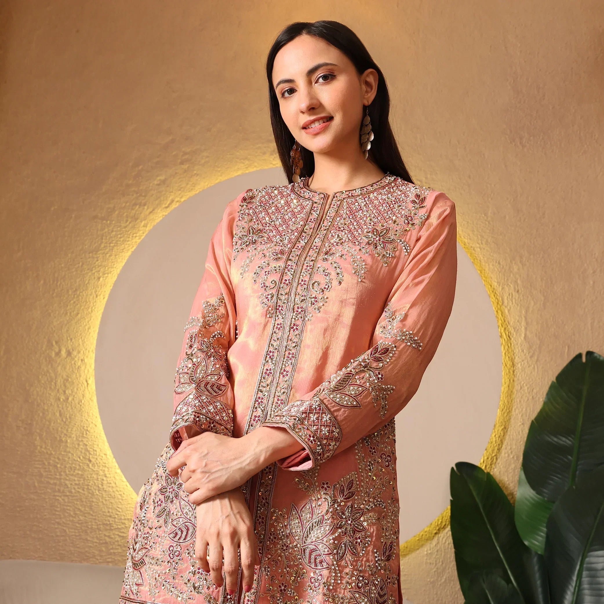 Woman in a peach Banarasi Anarkali suit with intricate embroidery, standing indoors
