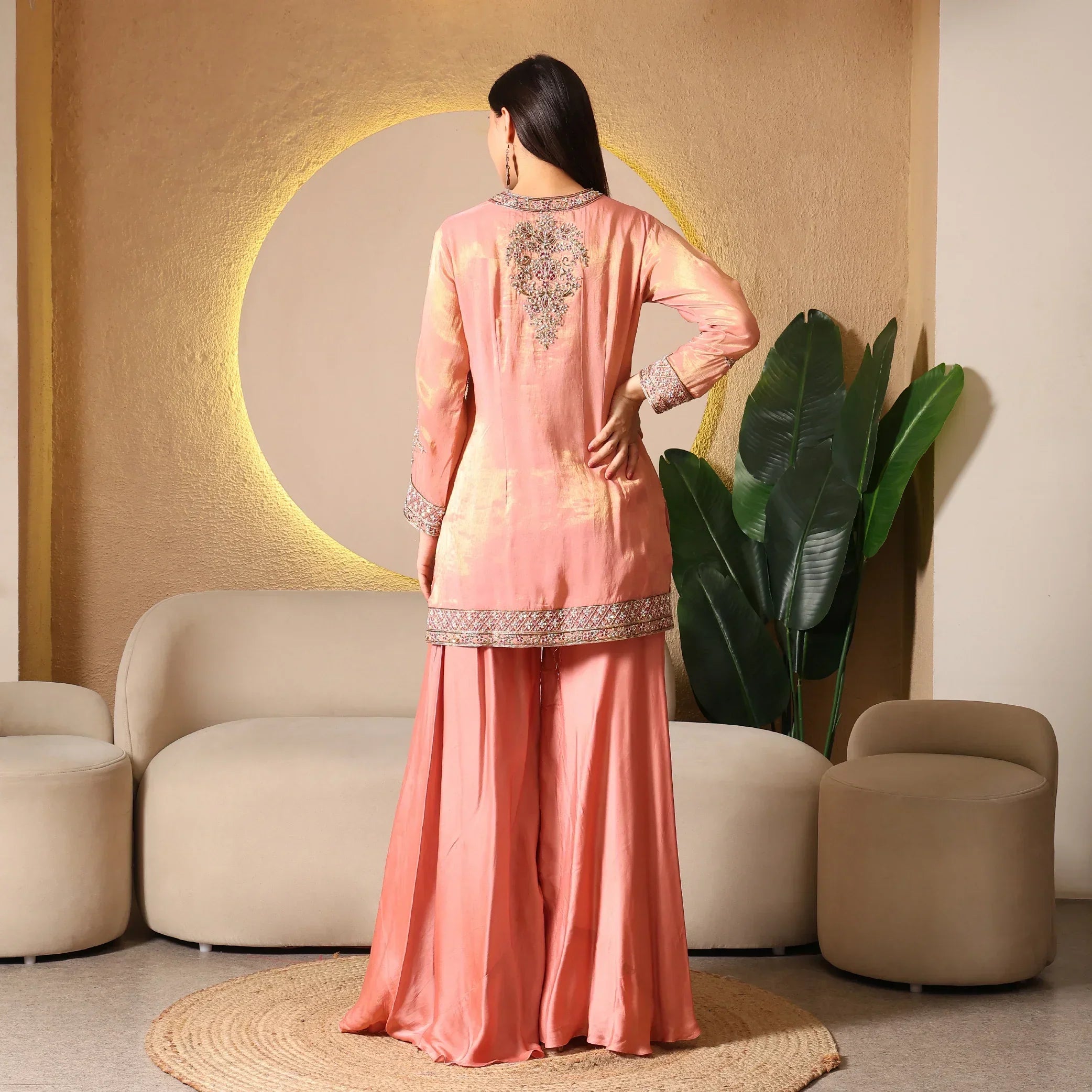 Woman in peach ethnic suit with embroidered detail, sharara pants, indoor modern setting