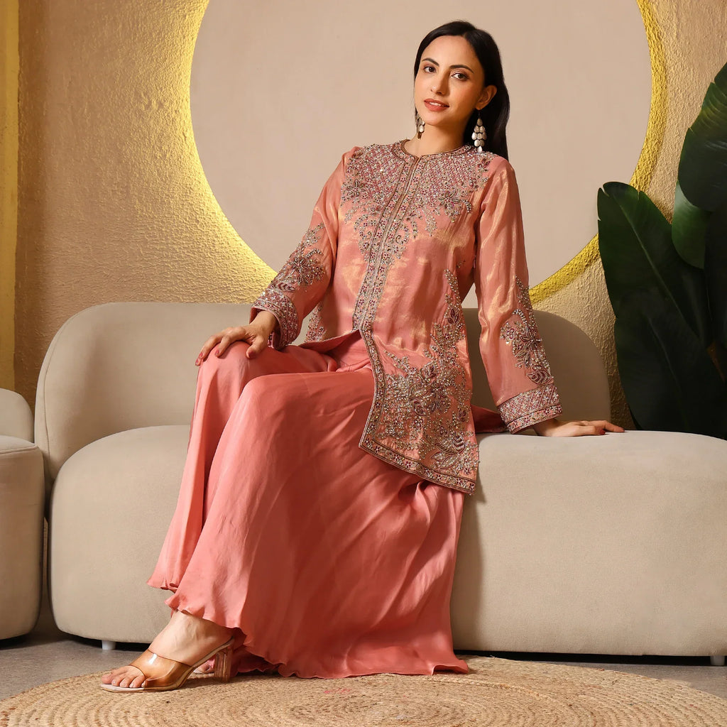 Woman in peach embroidered ethnic suit seated on beige sofa, festive outfit with heels