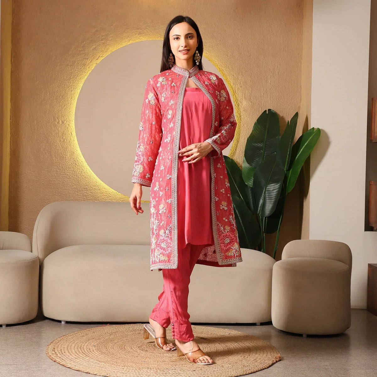 Woman in a pink embroidered ethnic suit with long jacket, posing in a modern living room