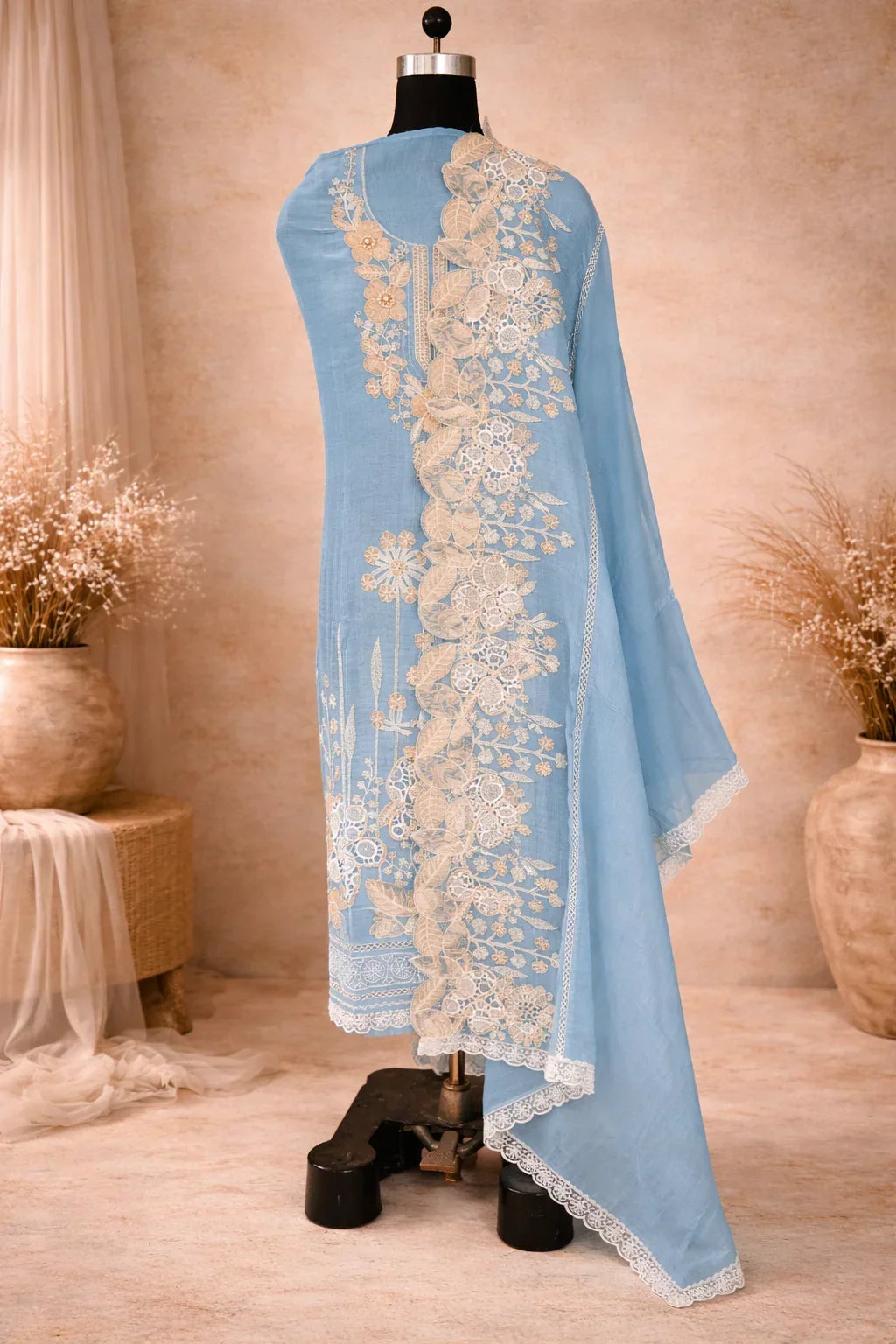 Light blue ethnic suit draped on mannequin with intricate beige floral embroidery and lace trim
