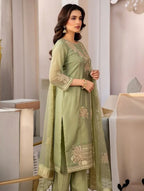 Woman wearing sage green embroidered Anarkali suit with sheer dupatta in elegant indoor setting