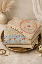 Beige ethnic wear fabric with colorful embroidery and lace, styled with bangles and flowers.