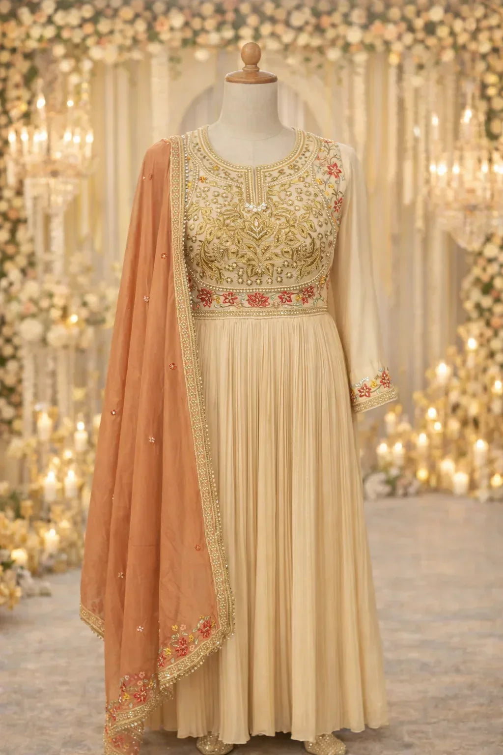 Ivory Anarkali suit with gold embroidery and peach dupatta, displayed on mannequin in elegant setting