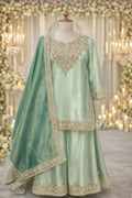 Pastel green ethnic Anarkali suit with intricate gold embroidery, dupatta and flared pants, displayed on a mannequin in an elegant festive setting.