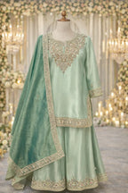Pastel green ethnic Anarkali suit with intricate gold embroidery, dupatta and flared pants, displayed on a mannequin in an elegant festive setting.