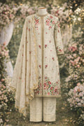 Ivory Banarasi three-piece suit with floral embroidery, dupatta, and straight pants, displayed in a floral outdoor setting.