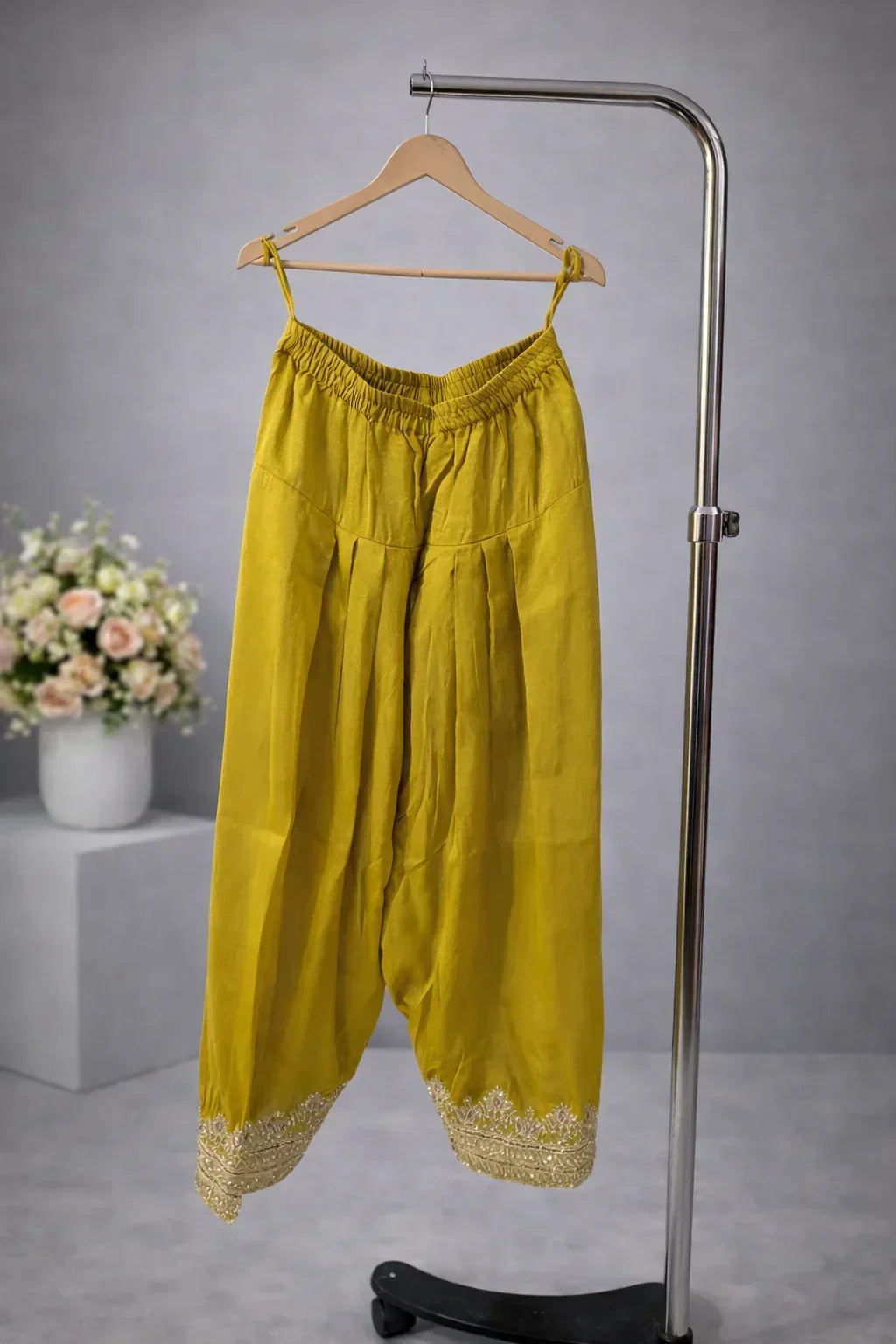 Mustard yellow ethnic palazzo pants with gold embroidery on hem, hanging on hanger